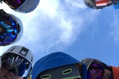 several skiers wearing gear and ski visors looking down at camera